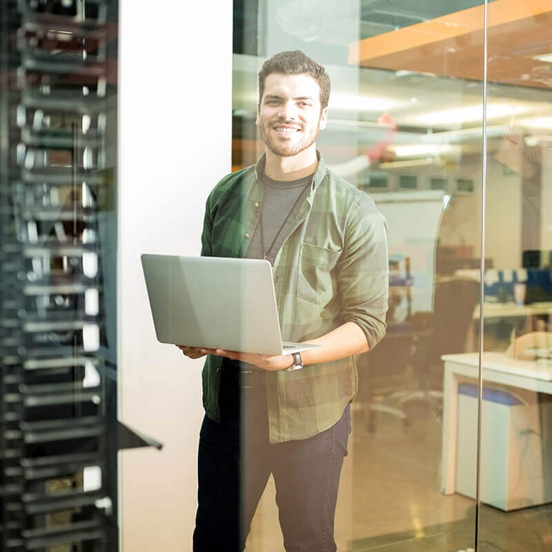 man standing holding laptop in server room