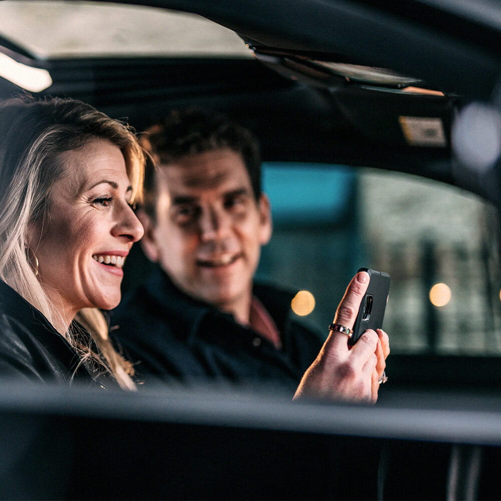 man and woman sitting in car looking at mobile phone