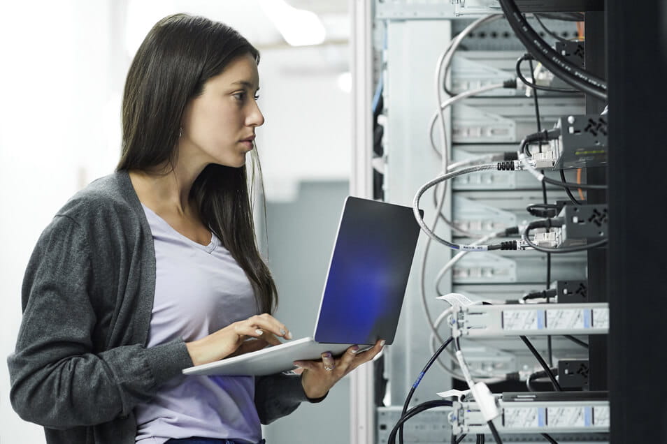 woman holding laptop and looking at server in front of her