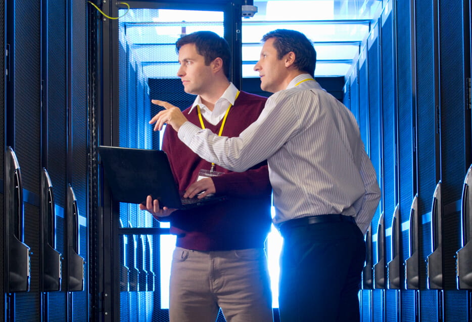 man holding laptop and man pointing to server in server room