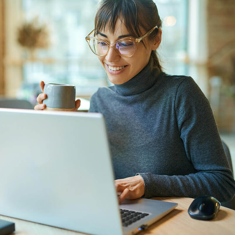 woman holding mug smiling down at laptop