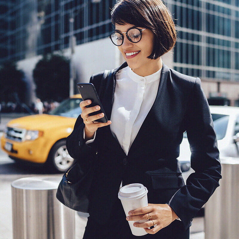 smiling woman holding coffee looking at phone