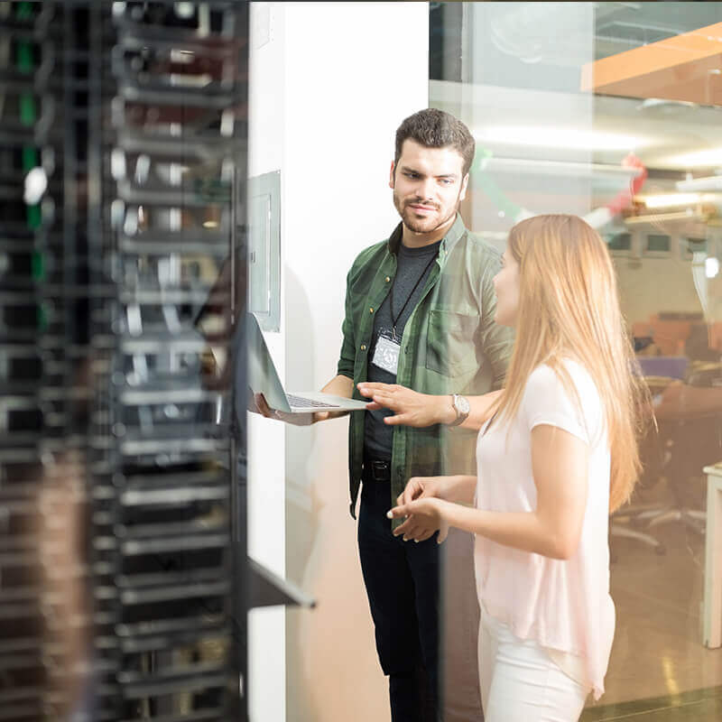 man holding laptop talking to woman in server room