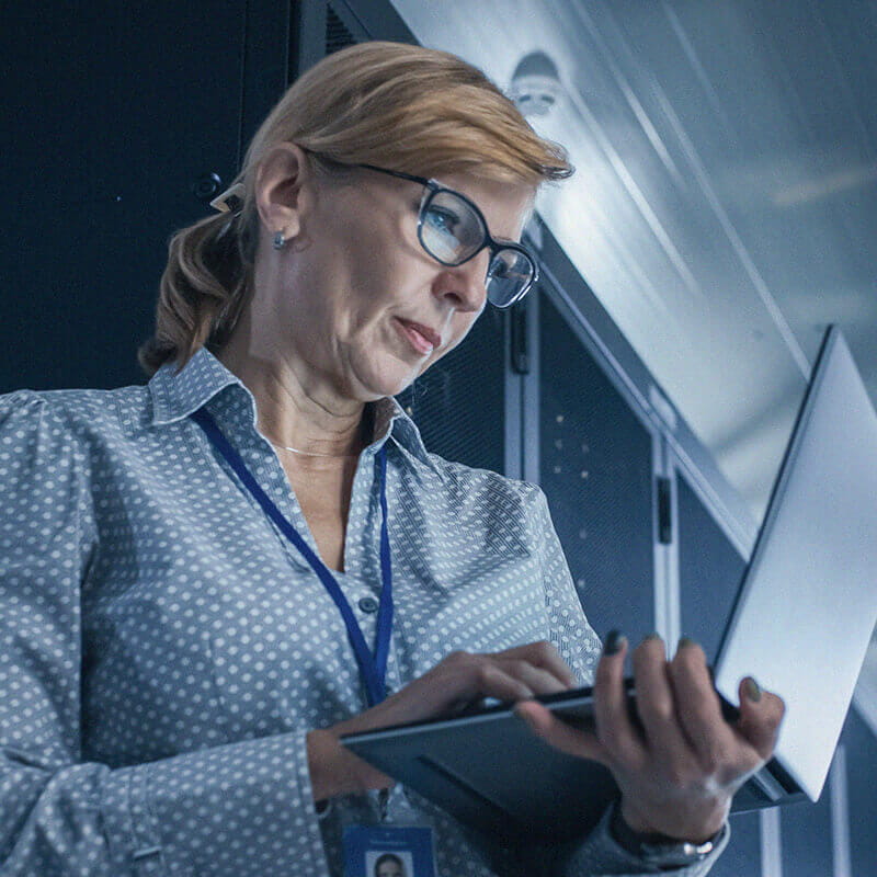 woman with glasses holding and looking down at laptop