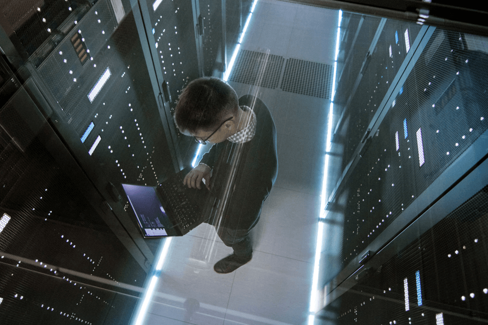 view from above of man in server room looking down at laptop